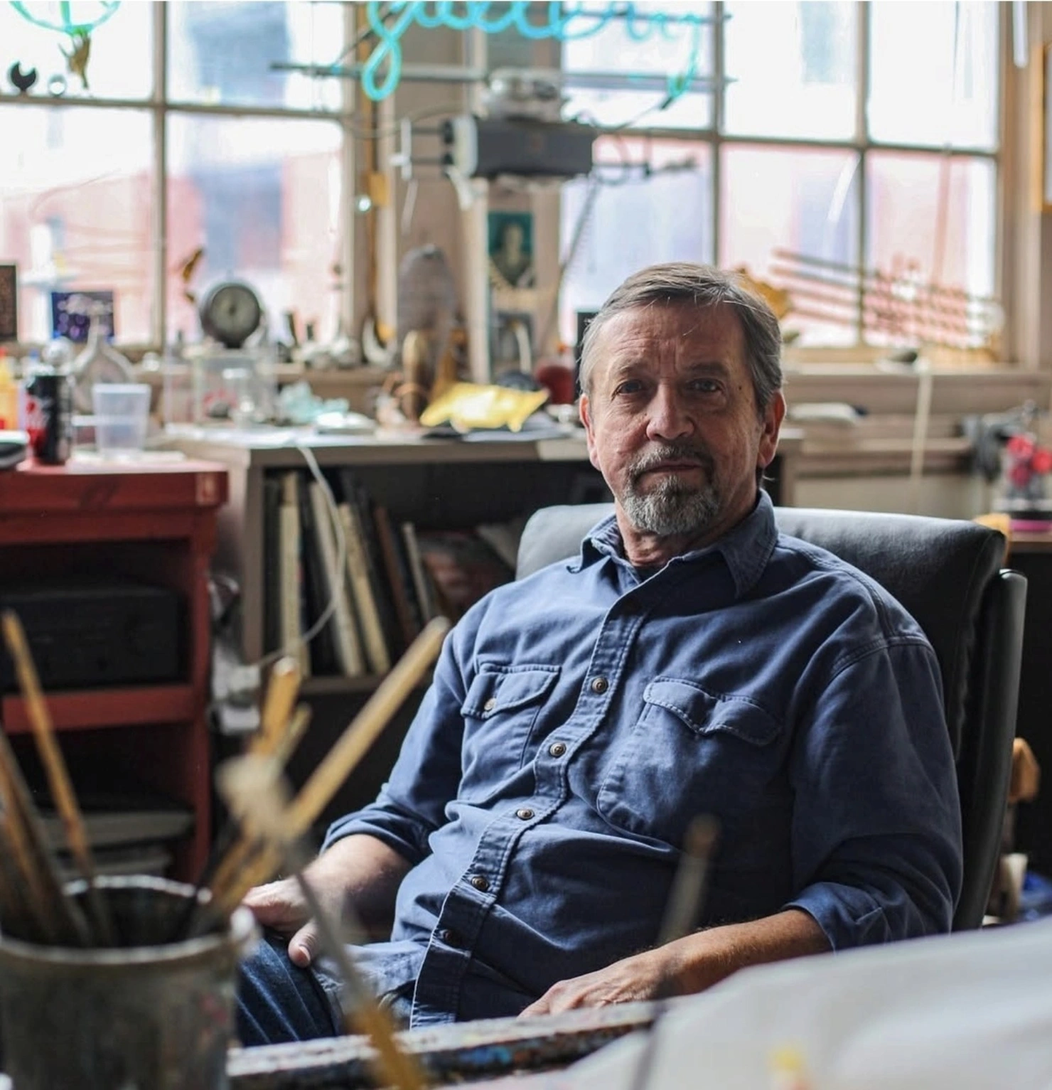David Airhart seated in his studio, surrounded by brushes and painting materials